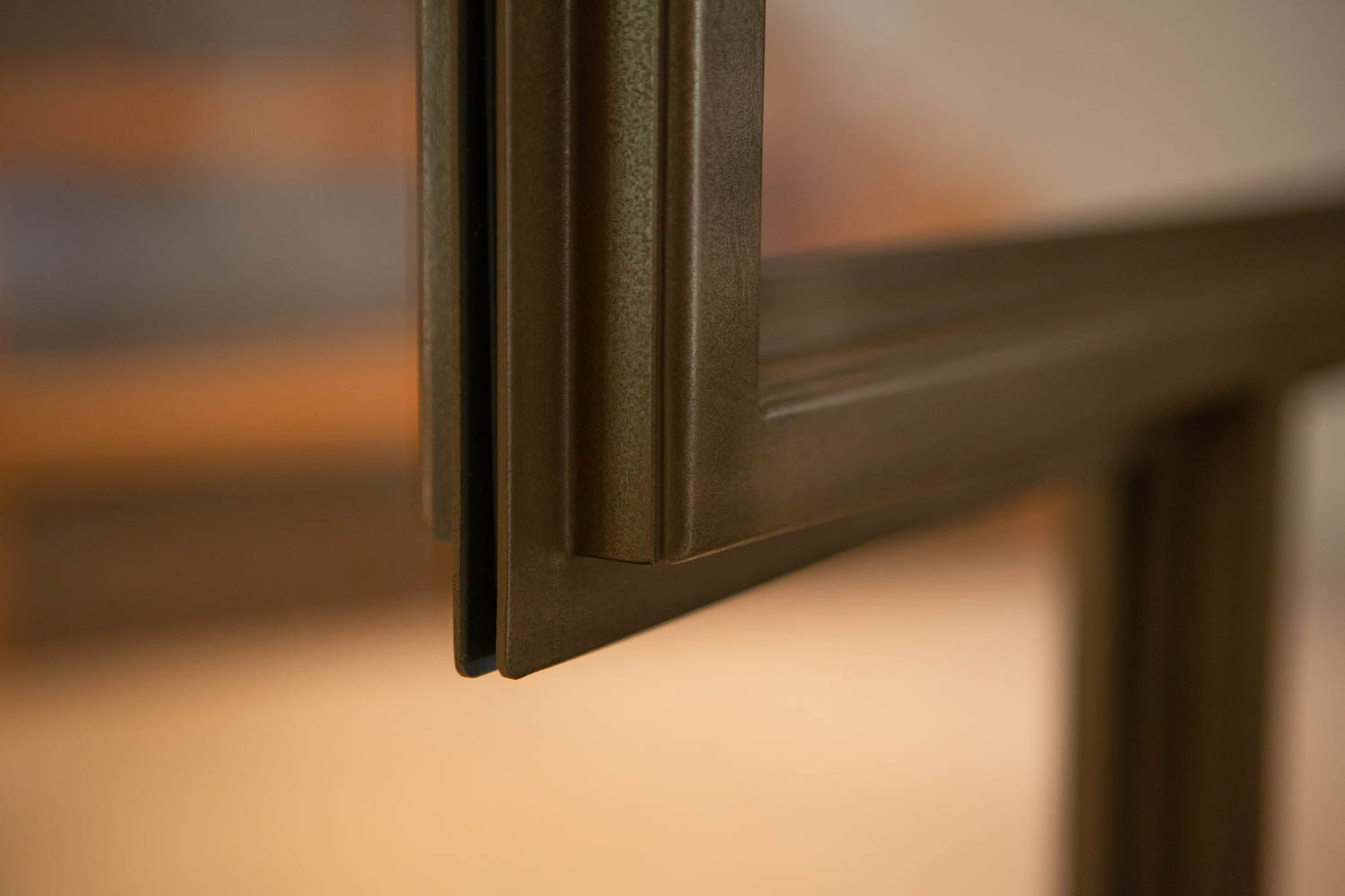 Detail van een bronzen stalen deur met verfijnde afwerking en slank profiel.